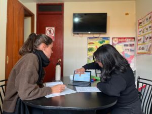 Local Cusqueña Spanish teacher demostrating Spanish lesson on Ipad to foreign European student in a brightly lit classroom with Spanish informational sheets on the walls.